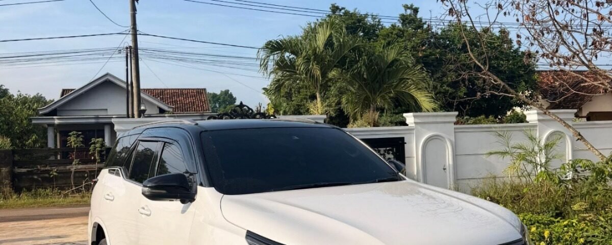 White Toyota SUV parked on a stone driveway in front of a house under a clear blue sky.