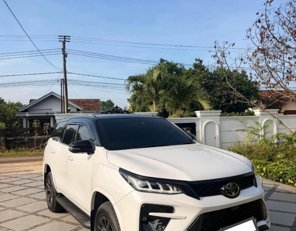 White Toyota SUV parked on a stone driveway in front of a house under a clear blue sky.