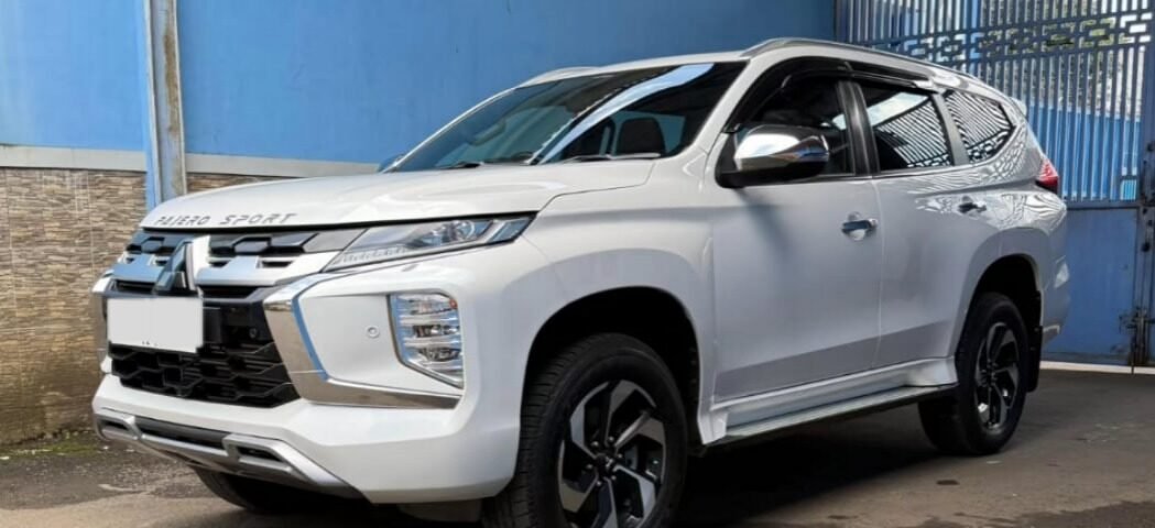 White Mitsubishi Pajero Sport parked under a metal carport beside a blue wall.