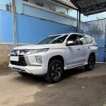 White Mitsubishi Pajero Sport parked under a metal carport beside a blue wall.