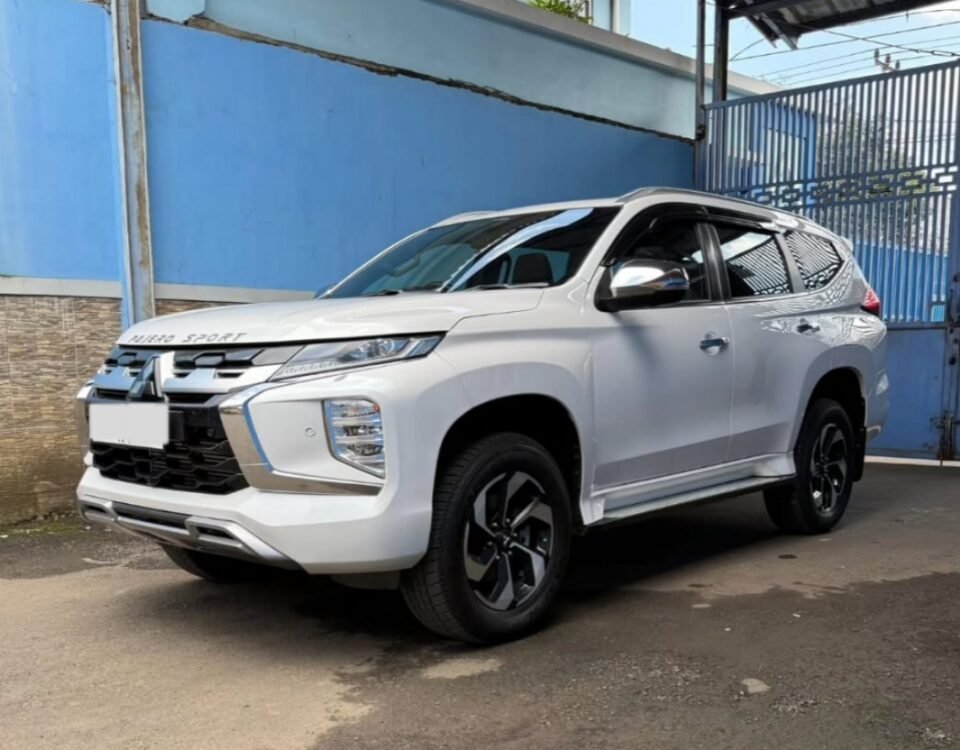 White Mitsubishi Pajero Sport parked under a metal carport beside a blue wall.