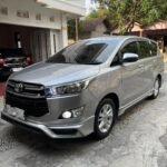 Silver Toyota minivan parked in a residential driveway, front-left angle of the vehicle