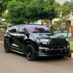 Black SUV parked on a street, glossy finish reflecting surrounding trees with a green urban backdrop behind it.