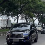 Black Toyota SUV driving on a tree-lined city street with other cars in the background