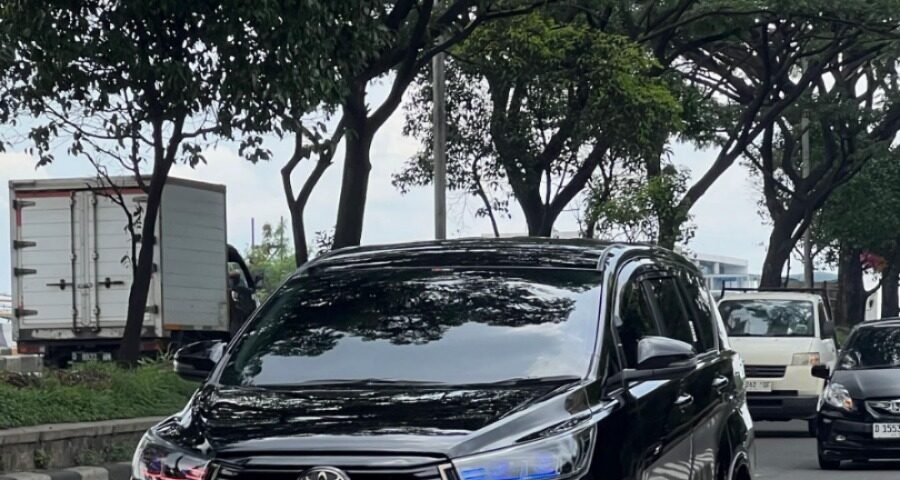 Black Toyota SUV driving on a tree-lined city street with other cars in the background