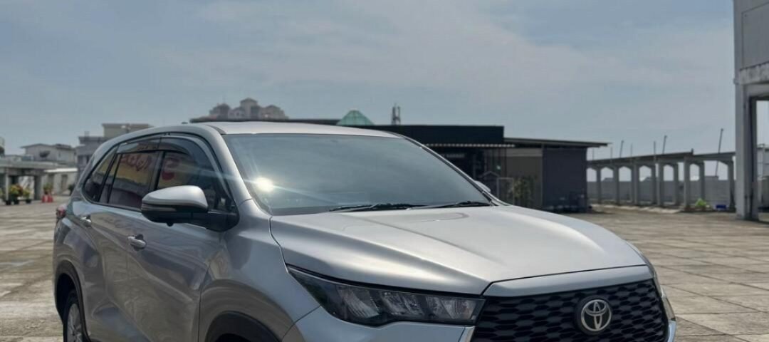 Silver Toyota SUV parked on a concrete open lot under a bright blue sky, front view.
