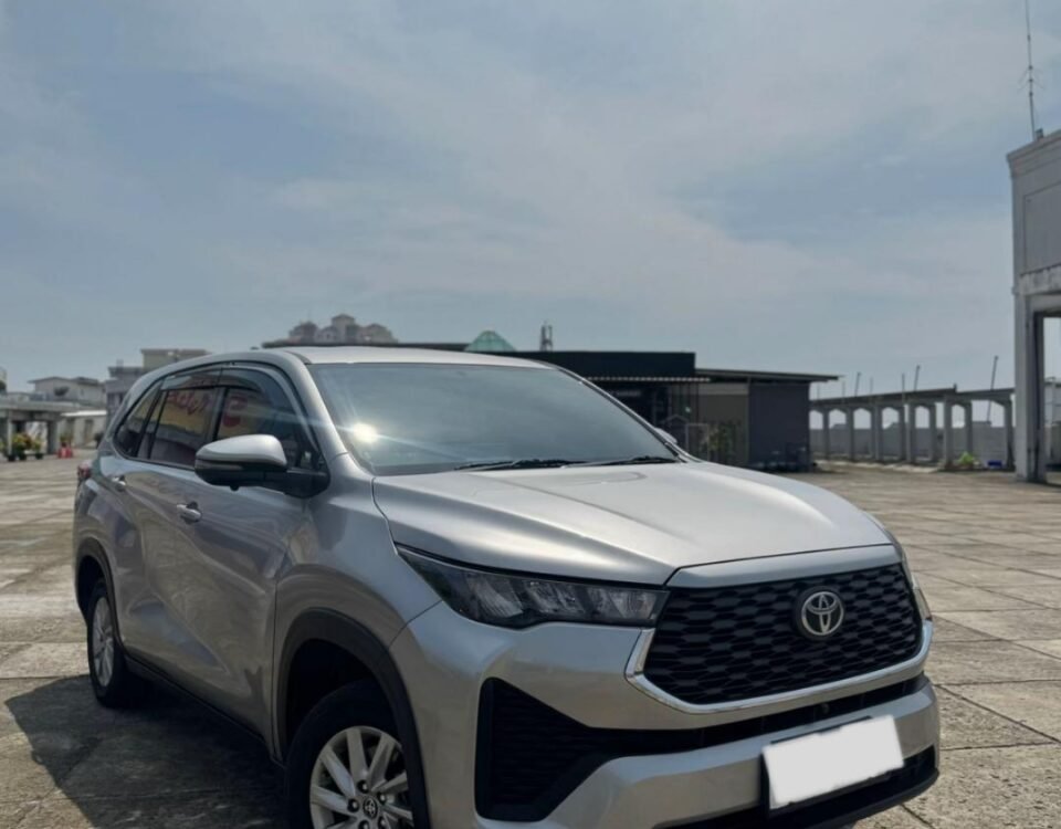Silver Toyota SUV parked on a concrete open lot under a bright blue sky, front view.