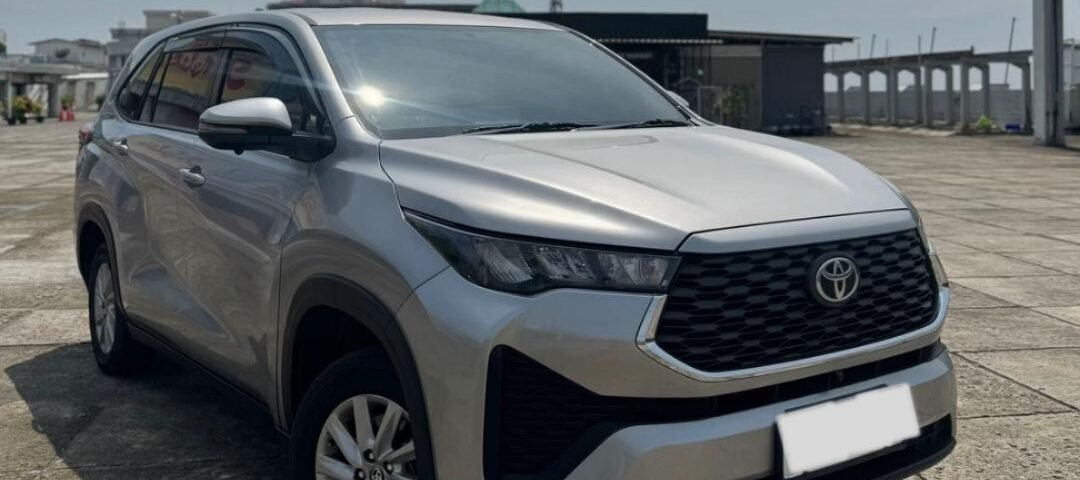 Front-left three-quarter view of a silver Toyota SUV parked on a paved lot with distant buildings in the background.