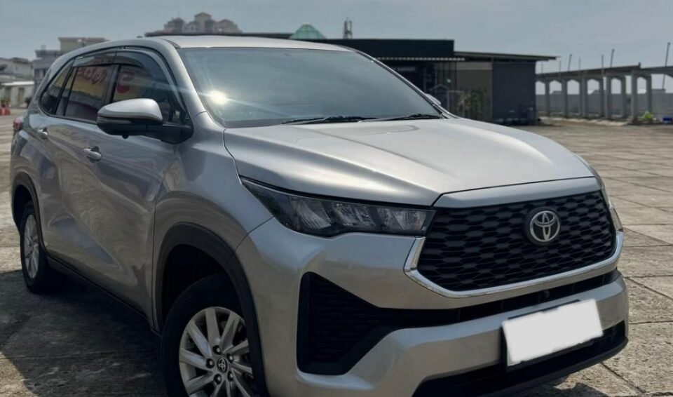 Front-left three-quarter view of a silver Toyota SUV parked on a paved lot with distant buildings in the background.