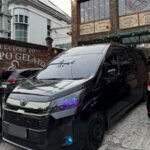 Black Toyota van parked in front of a brick gelato shop with a large clock window.