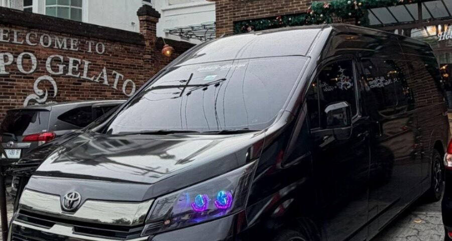 Black Toyota van parked in front of a brick gelato shop with a large clock window.