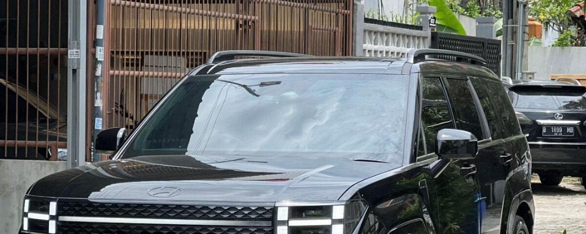 Front three-quarter view of a black SUV parked on a brick driveway with a gated building in the background and overhead power lines.