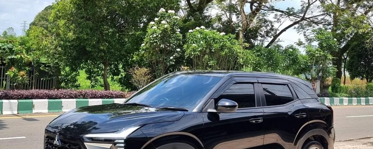 Black SUV parked on a street with green trees and a blue sky in the background, front view angled to the left