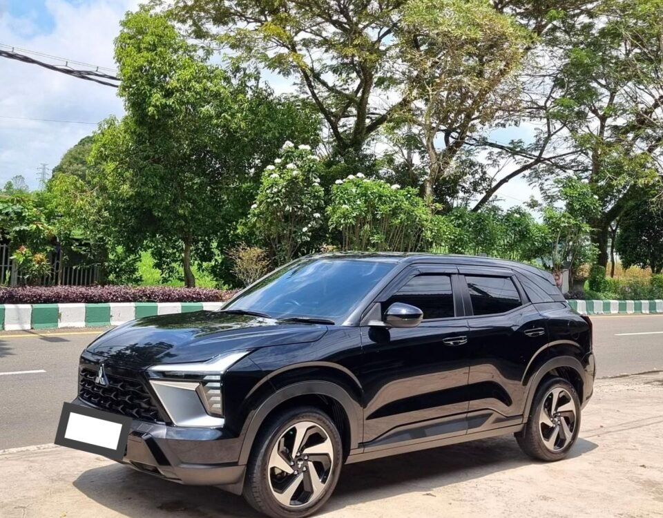 Black SUV parked on a street with green trees and a blue sky in the background, front view angled to the left