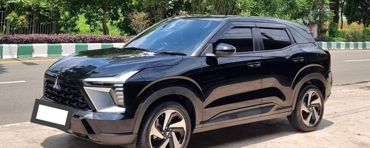 Black SUV parked on a street with green trees and a blue sky in the background, front view angled to the left
