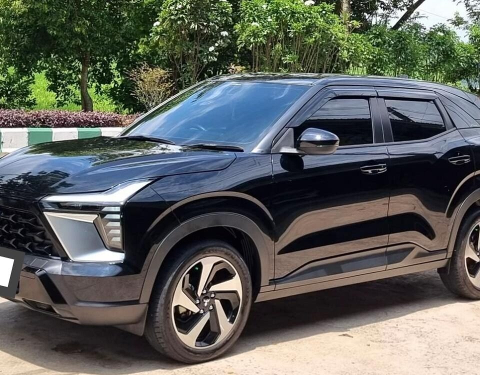 Black SUV parked on a street with green trees and a blue sky in the background, front view angled to the left