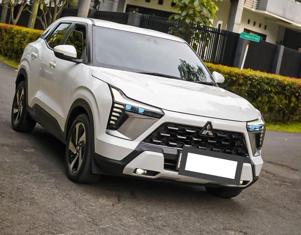 White Mitsubishi SUV parked at an angle on a residential street with a modern two-story house and trees in the background.