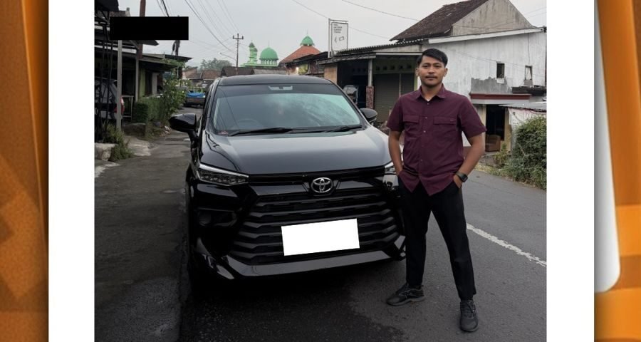 Man in a maroon shirt stands beside a black Toyota SUV parked on a wet street in a small town neighborhood.