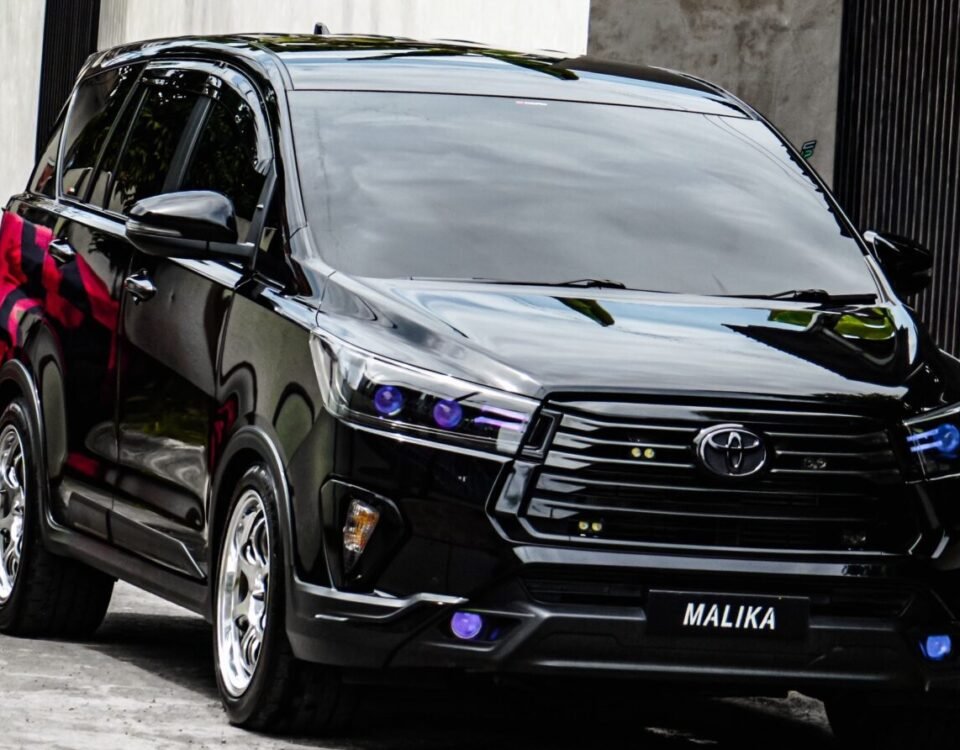 Black Toyota SUV parked in a narrow alley, banana trees and concrete walls in the background; license plate reads MALIKA.