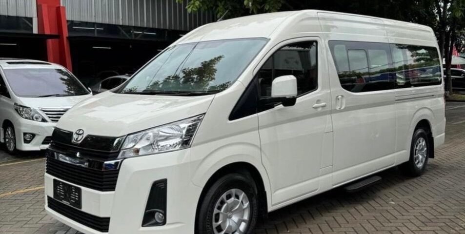 White passenger van parked on a brick parking lot with green trees in the background.