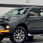 Showroom scene with a dark-colored Toyota SUV, close-up of front and side, glossy reflections and neon ceiling lights above