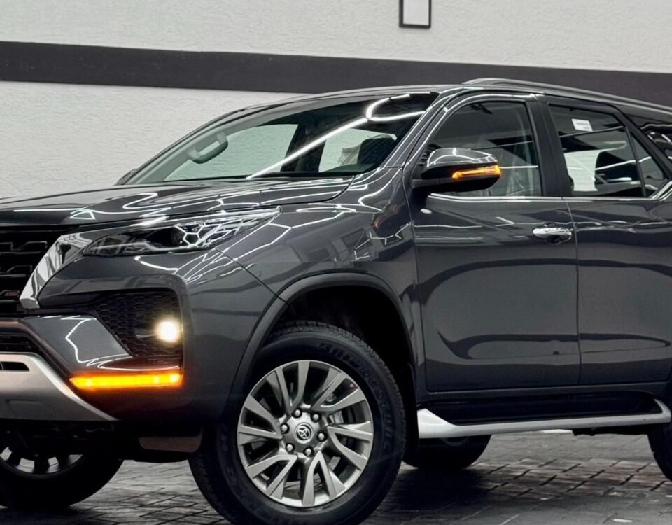 Showroom scene with a dark-colored Toyota SUV, close-up of front and side, glossy reflections and neon ceiling lights above