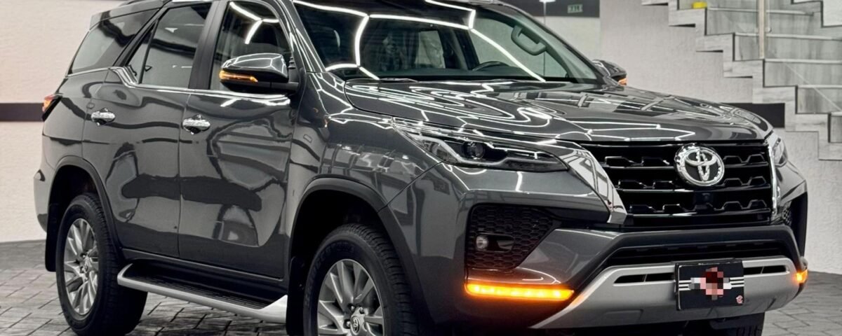 Black SUV on a showroom floor with a glass-railed staircase and bright geometric ceiling lights in the background.