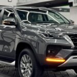Black SUV on a showroom floor with a glass-railed staircase and bright geometric ceiling lights in the background.
