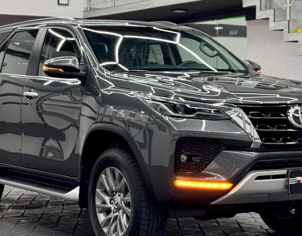 Black SUV on a showroom floor with a glass-railed staircase and bright geometric ceiling lights in the background.