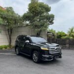 Black SUV parked in a parking lot beside a gray concrete wall under a cloudy sky on an overcast day.