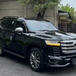 Black SUV parked in a parking lot beside a gray concrete wall under a cloudy sky on an overcast day.