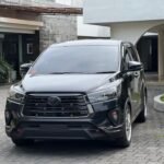 Front view of a dark gray Toyota SUV parked on a brick driveway in front of a modern building complex