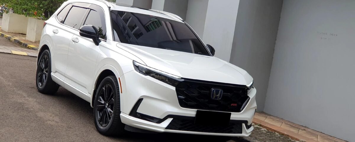 White Honda SUV parked on a street beside a gray building, angled front-side view with black wheels and tinted windows.