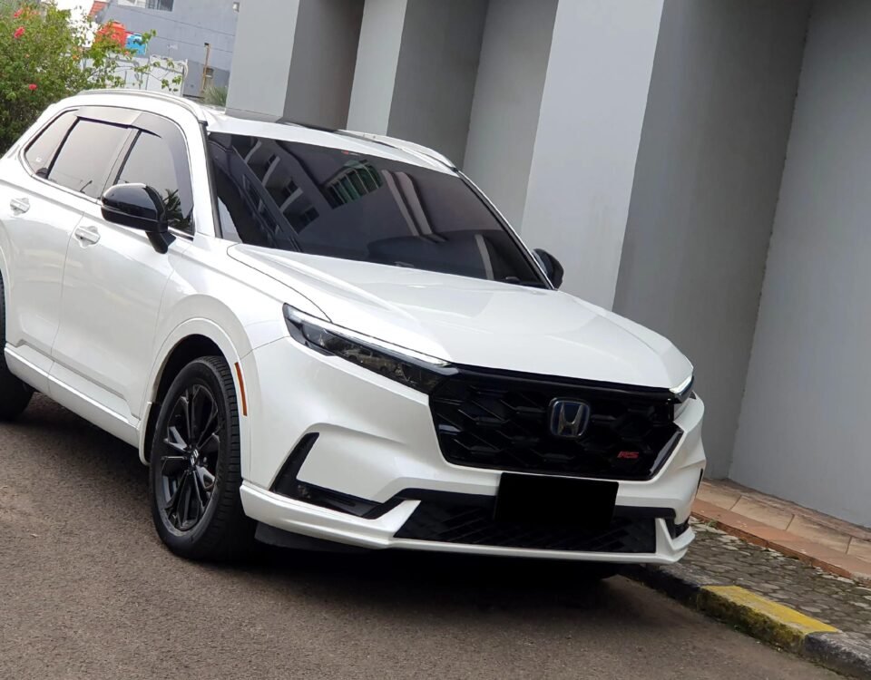 White Honda SUV parked on a street beside a gray building, angled front-side view with black wheels and tinted windows.