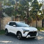 White Mitsubishi SUV parked on a paved driveway with palm trees and a stone wall behind it.