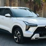 White Mitsubishi SUV parked on a paved driveway with palm trees and a stone wall behind it.