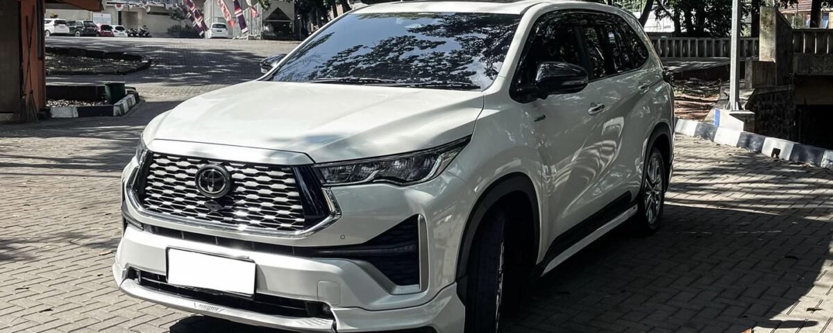 White SUV parked on a brick driveway beneath leafy trees with a building in the background.