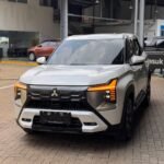 White Mitsubishi SUV parked at a dealership lot, front view with illuminated orange daytime running lights