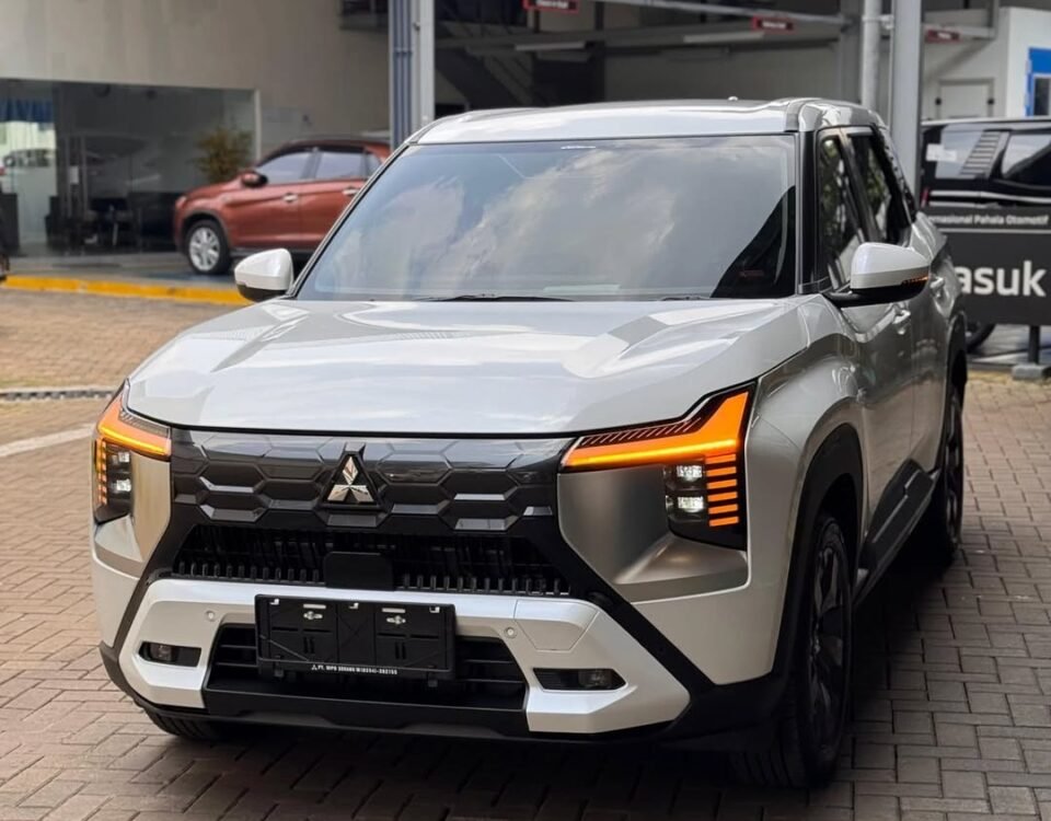 White Mitsubishi SUV parked at a dealership lot, front view with illuminated orange daytime running lights
