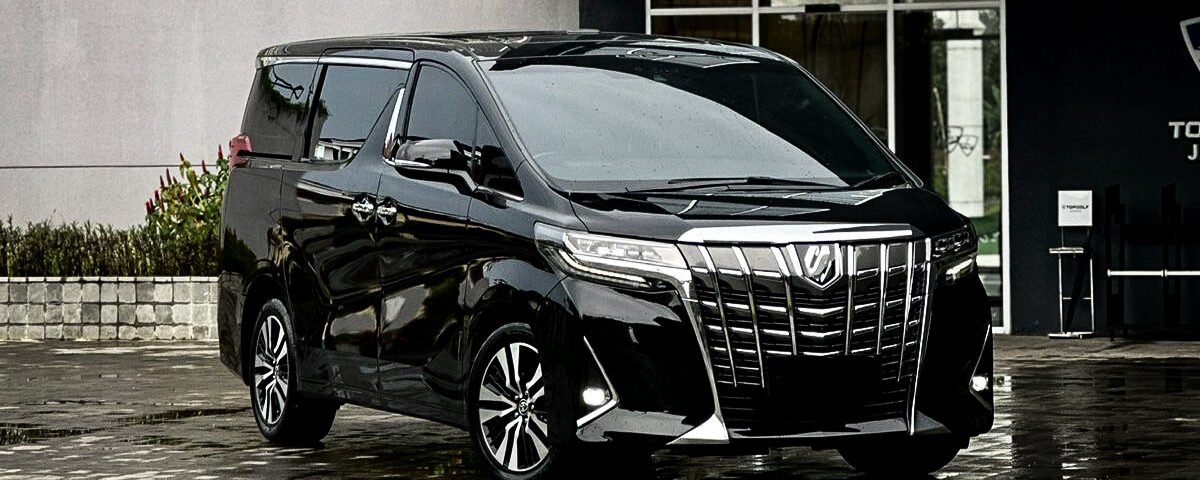 Black luxury minivan parked on a wet, reflective pavement outside a modern building with large glass windows.