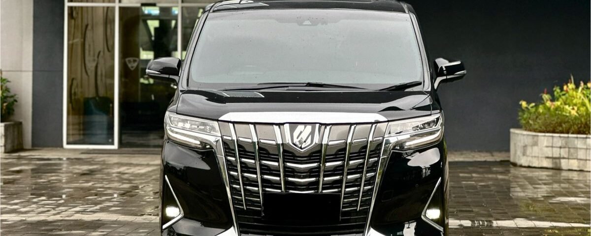 Front view of a shiny black minivan with a large chrome grille parked outside a building.