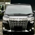 Front view of a shiny black minivan with a large chrome grille parked outside a building.