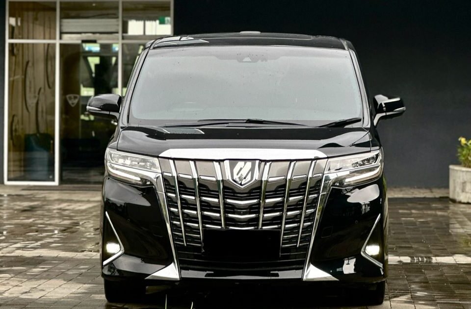 Front view of a shiny black minivan with a large chrome grille parked outside a building.