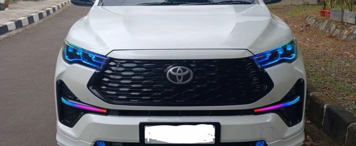 snaptik_7593942426075680007_1_v2 - Dyantransport Front view of a white Toyota SUV parked on a street, blue LED headlights glowing, urban backdrop with power lines.