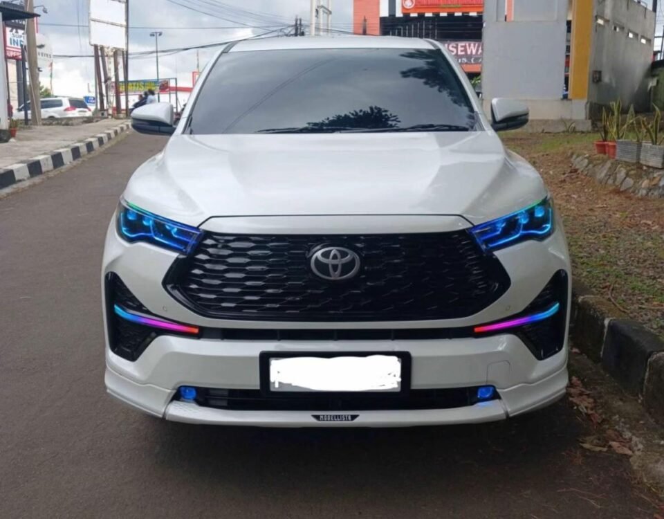 Front view of a white Toyota SUV parked on a street, blue LED headlights glowing, urban backdrop with power lines.