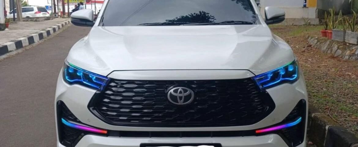 White Toyota SUV facing camera with blue accent headlights, parked on a city street with urban storefronts in the background