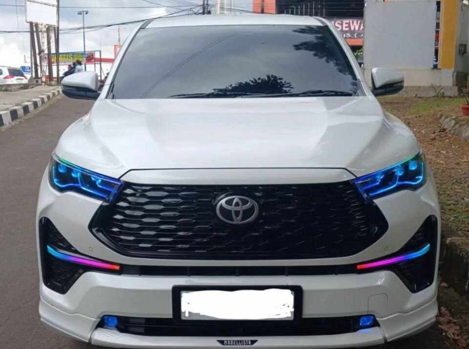 White Toyota SUV facing camera with blue accent headlights, parked on a city street with urban storefronts in the background