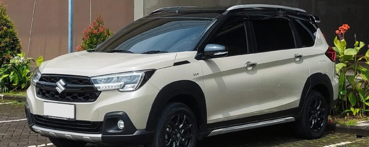 White Suzuki SUV parked in a lot, front-left three-quarter view with greenery around it