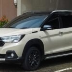 White Suzuki SUV parked in a lot, front-left three-quarter view with greenery around it