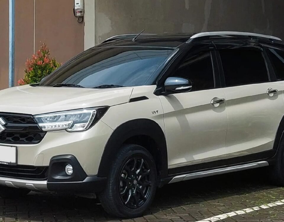 White Suzuki SUV parked in a lot, front-left three-quarter view with greenery around it